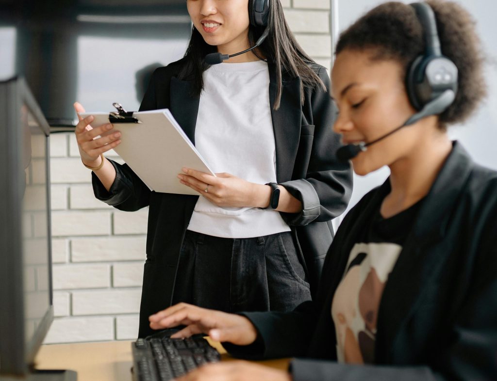 Two women in a call center working with headsets and computers, focusing on customer support.